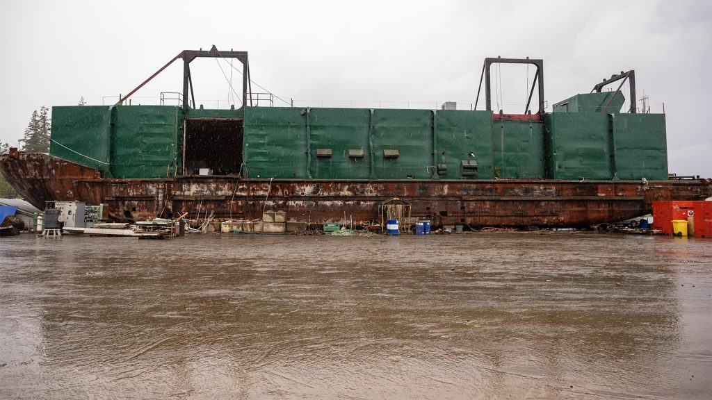 A large barge sits on a beach in the rain.